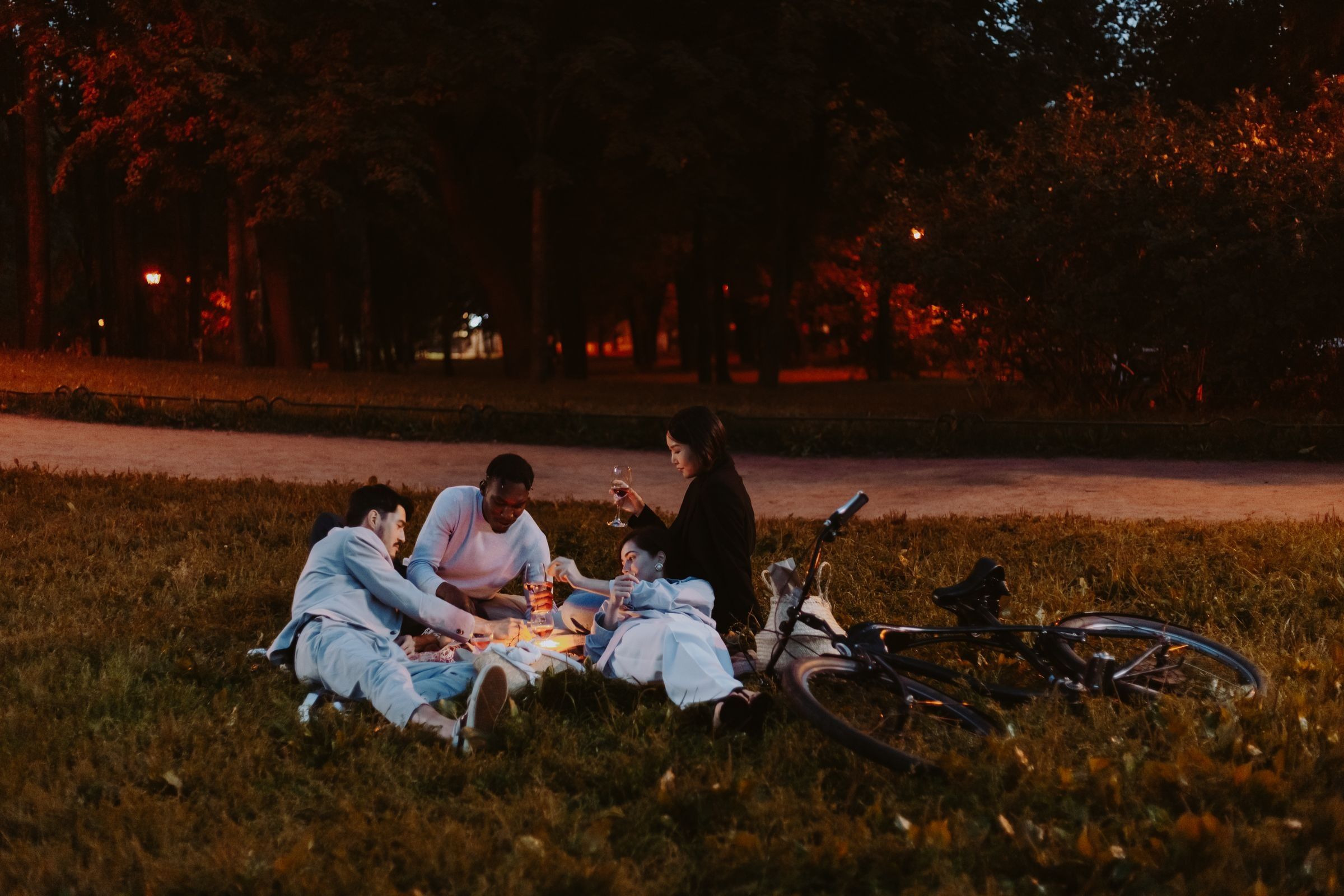 Five people sitting together on a park lawn at twilight, bikes lying in the grass.