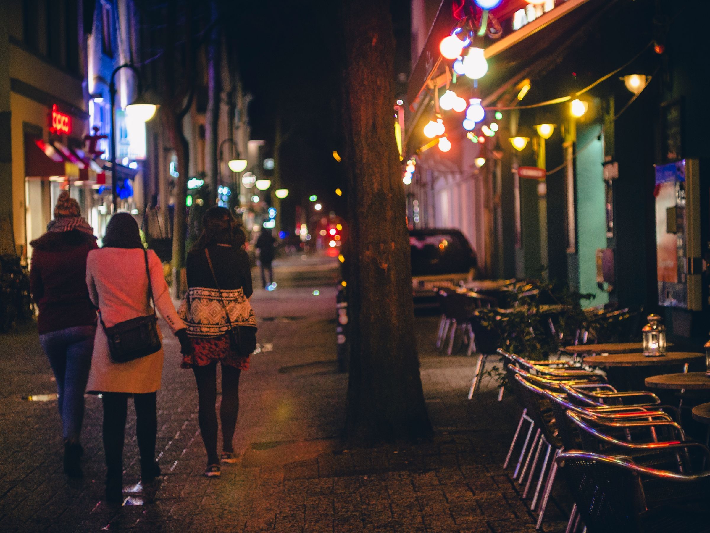 Three people walking away down a city street at night under string lights.