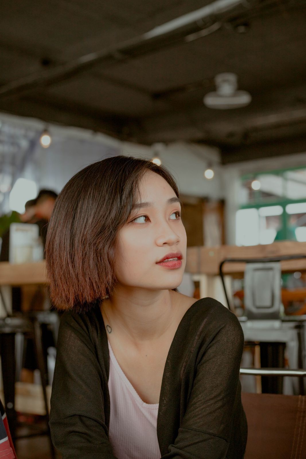 A young woman in a cafe, looking to the right with a small smile.