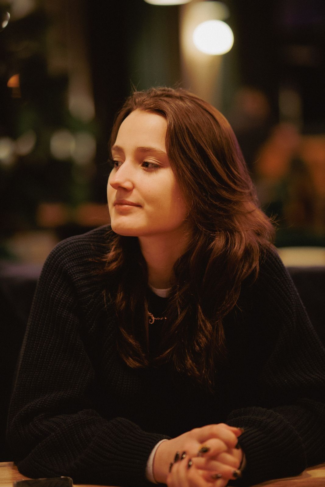 A young woman at a cafe table in warm light, looking to the left.